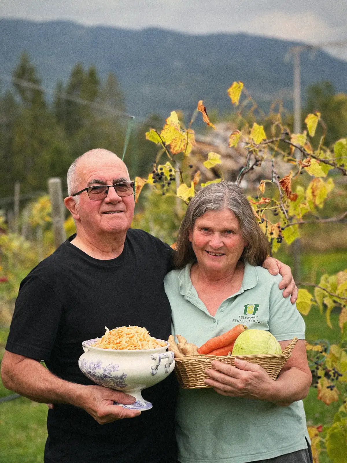 Berit og Freddy smiler i hagen, han med en bolle kimchi, hun med en kurv kål og gulrøtter