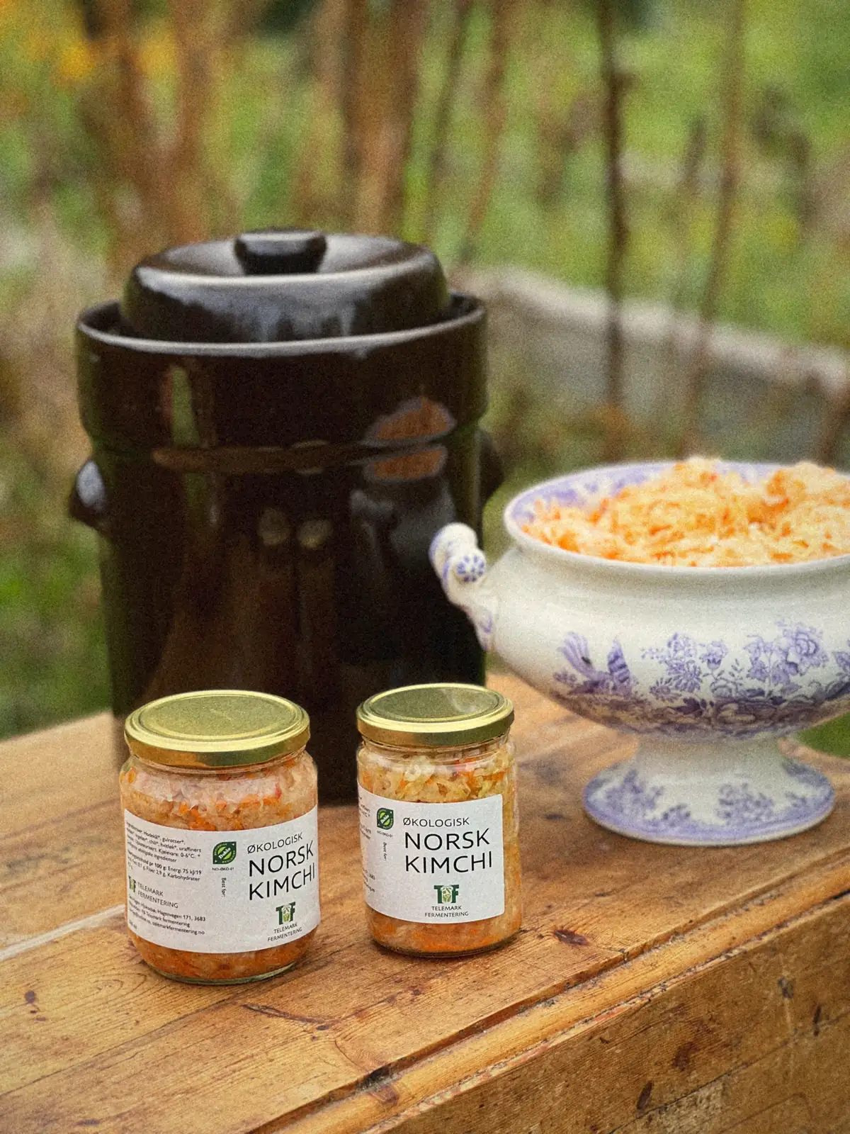 To glass kimchi på arbeidsbordet ute, med fermenteringskrukka og en terrin med kimchi bak